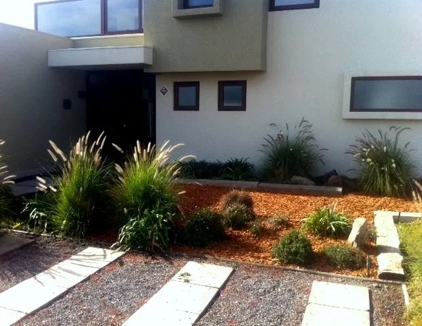 Antejardín de una casa con gramíneas, mulch rojo y gravilla