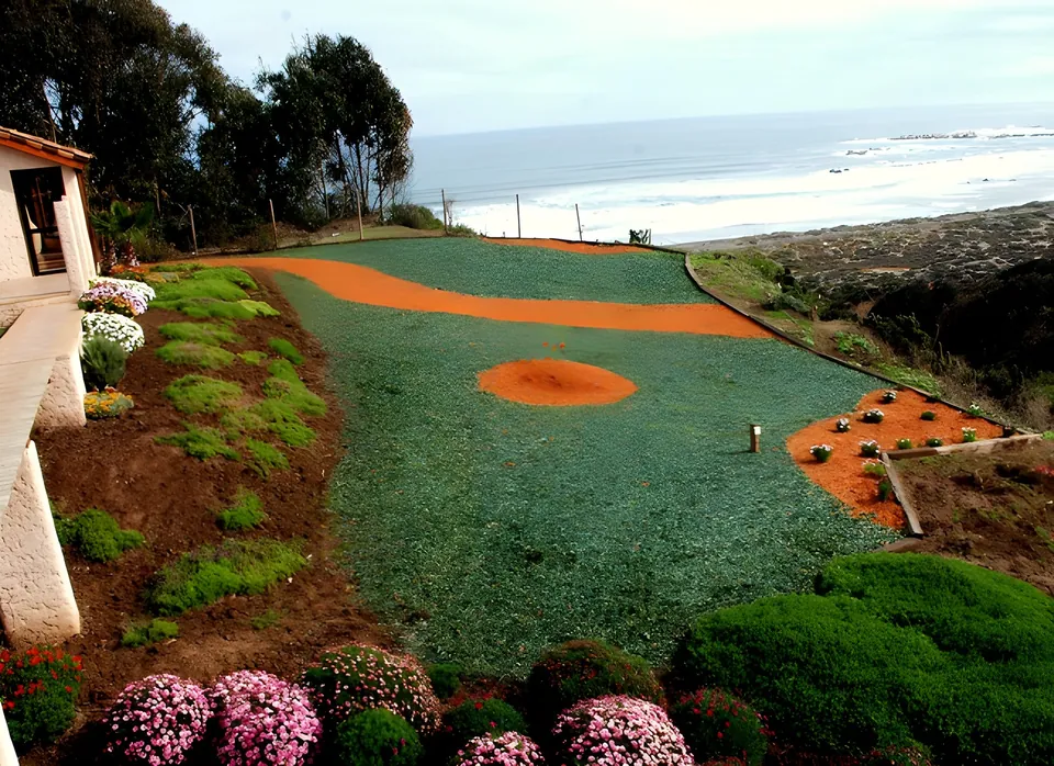Ladera frente al mar con figuras de mulch naranjo sobre cubresuelo