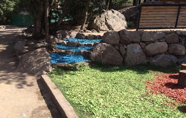 Mulch azul entre rocas que simula un curso de agua en un parque
