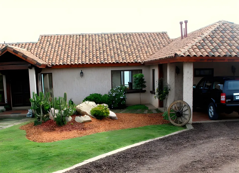 Antejardín con mulch rojo, cactus y rocas blancas frente a una casa con techo de teja