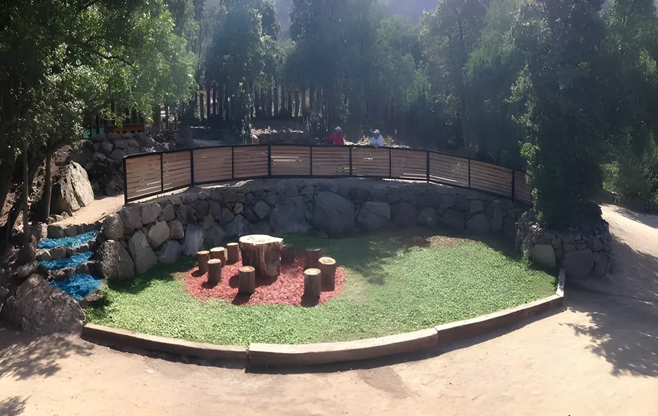 Anfiteatro de piedra con pasto y un círculo de mulch rojo con asientos de tronco